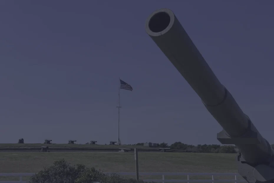 Close-up of a large artillery cannon barrel pointed skyward with a row of cannons and an American flag in the background on a field.