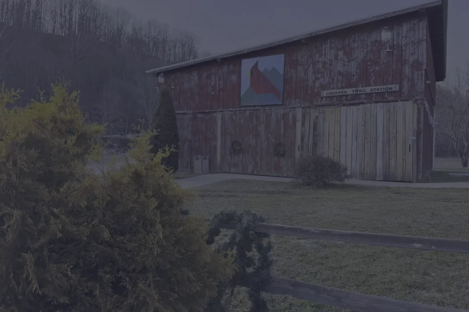 Weathered red station building with a mountain mural and a Creeper Trail Station sign, framed by a wooden fence and surrounding bushes.