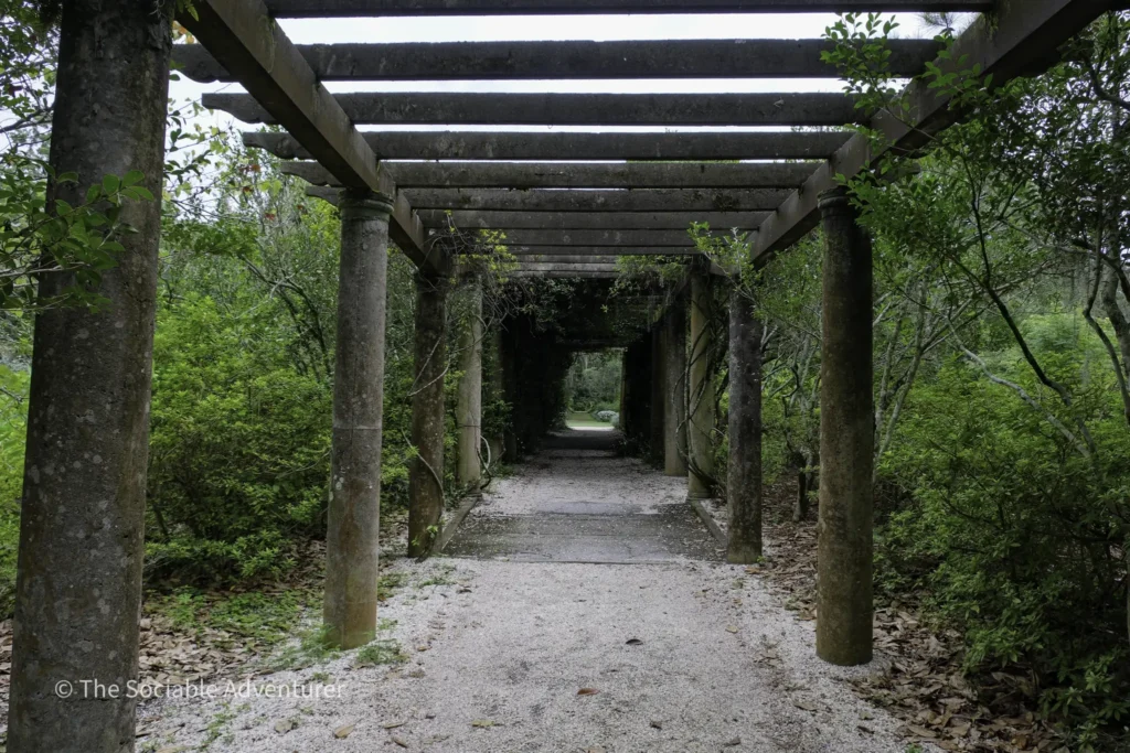 Stone pergola with mossy columns forming a shaded gravel path through a lush garden.