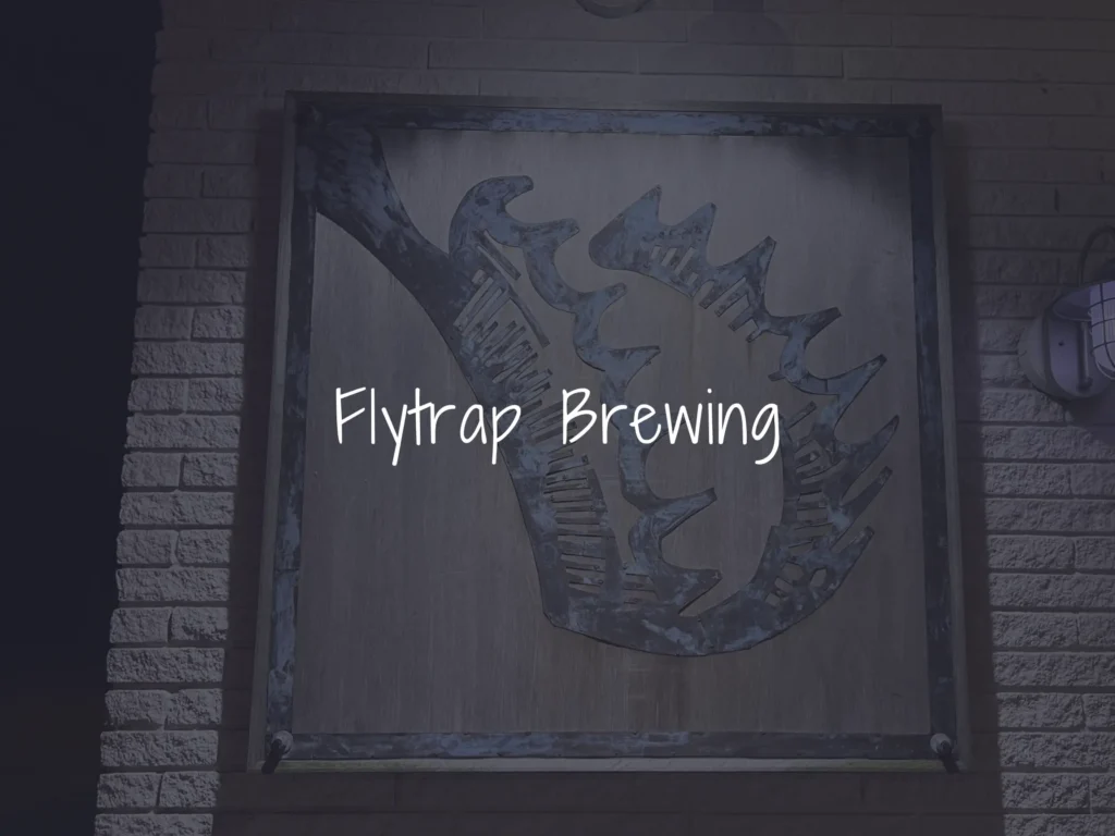 Weathered wooden sign on a brick wall with a blue logo and the text 'Flytrap Brewing'.