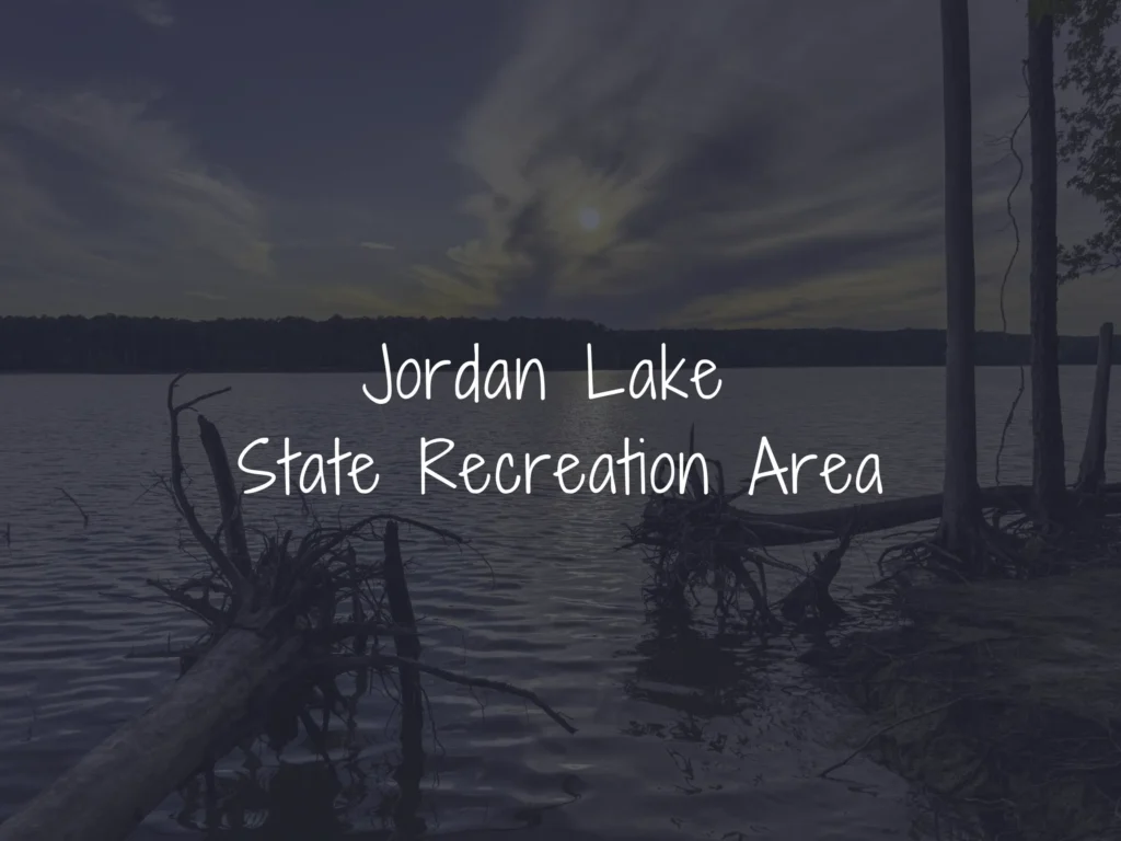Sunset over a lake with silhouetted trees and a log in the foreground; large handwritten text reads 'Jordan Lake State Recreation Area'